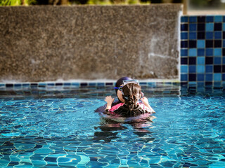 little daughter hugging with mother while standing together in a swimming pool at a tropical resort
