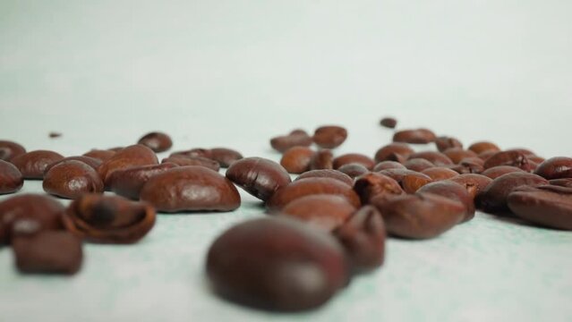 Person throws aromatic brown roasted coffee grains onto white table surface at artificial light in studio room macro