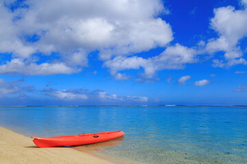 An orange kayak on a beach, with a beautiful blue tropical lagoon behind it. Aroa Beach, Rarotonga, Cook Islands