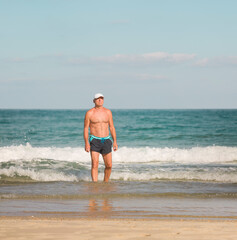 Fototapeta na wymiar A beautiful mature man is standing in the sea and sunbathing