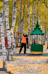 A man sweeps yellow leaves in an autumn park on a playground