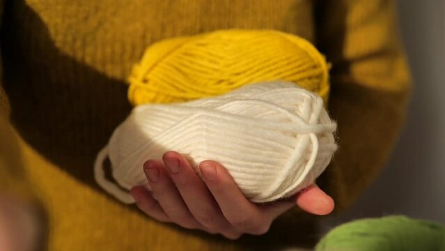 Knitting concept. Skeins of yarn of different colors in female hands in a brown wool sweater.Wool yarn in yellow, beige, purple and green.Hobby and needlework concept. Knitting warm clothes 