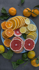 sliced ​​citruses - grapefruit, orange, tangerine and lemon in a blue plate on a concrete background