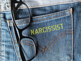 Reading glasses in jeans pocket with yellow screen text NARCISSIST, concept of self-centered arrogant people who lack of empathy and consideration for others, excessive need for admiration