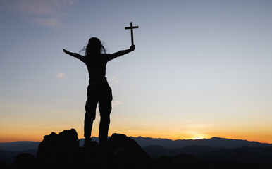 Silhouette of christian young woman praying with a  cross at sunrise, Christian Religion concept...
