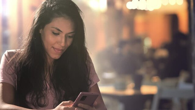 girl sits at the cafe outdoor using smart phone mobile at night,young arab woman browsing watching social media content on smartphone