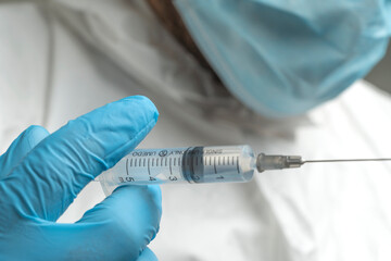 Doctor in a medical mask and cap looking at a syringe with a vaccine or medicine close-up
