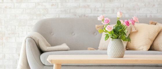 Beautiful rose flowers in vase on table and grey sofa in living room