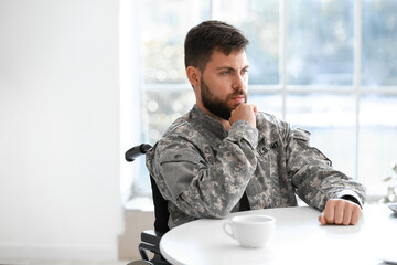 Naklejka premium Thoughtful young soldier in wheelchair at table in kitchen