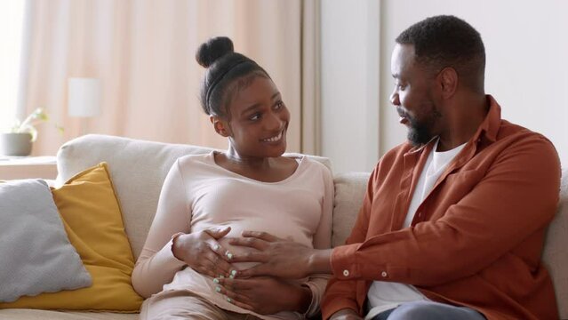 Happy young african american man and pregnant woman caressing belly and talking to each other, tracking shot, free space