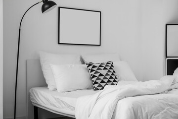 Comfortable bed with pillows, lamp and blank frame on light wall