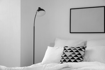 Comfortable bed with pillows, lamp and blank frame on light wall