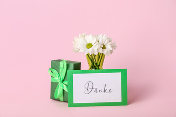 Card with text DANKE, gift box and flowers on pink background