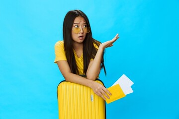 Asian woman traveling with yellow suitcase and tickets with passport in hand, tourist traveling by plane and train with luggage on blue background