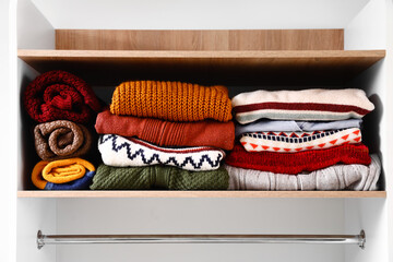 Warm knitted sweaters on shelf in wardrobe, closeup