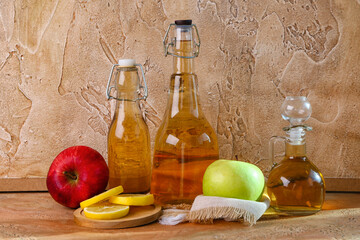 Bottles of apple cider vinegar and fruits on color table
