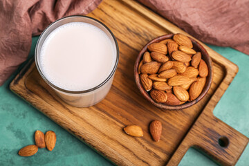 Wooden board with glass of almond milk and nuts on color background, closeup