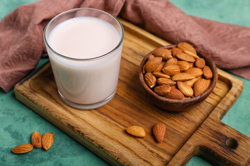 Wooden board with glass of almond milk and nuts on color background, closeup