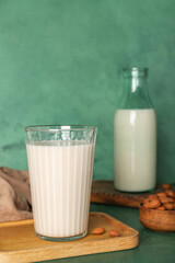 Wooden board with glass of almond milk and nuts on color background, closeup