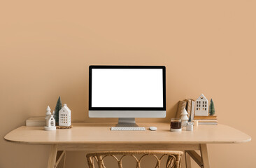 Workplace with computer, candle holders and Christmas trees near beige wall