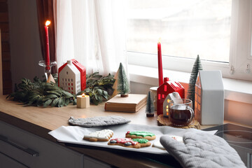 Candle holders with Christmas decor, cup of tea and cookies on counter in kitchen