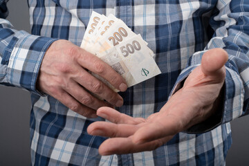 Man Ask gesture and holding Czech koruna in various nominal banknotes CZK. cash money on hand. Czechia finance concept. Close up selective focus.