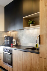 Kitchen in a modern mix of natural wood and black panels. Coffee maker and electric tea kettle on the kitchen counter,  domestic living concept.
