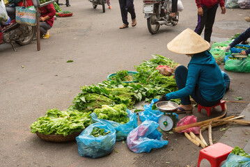 Vietnamese woman with traditional hat selling vegetables at market　ベトナムの市場で野菜を売るノンラーを被った女性