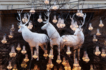 New Year Christmas exteriors. White huge decorative deer in decoration of branches and glowing chandeliers. Christmas decoration on old house background in downtown. Chic luxury designer decorations
