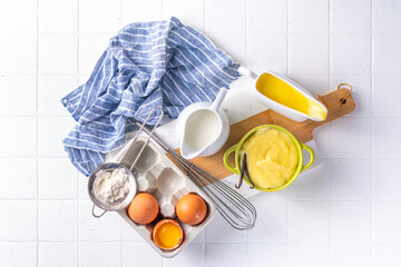 Homemade custard creme with ingredients - vanilla, milk and eggs. Sweet Creme anglaise dessert cooking background, on white kitchen table copy space
