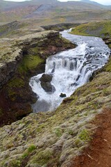 Naklejka na ściany i meble Majestic Icelandic Water fall with green moss and Lava rocks between cliff formation. damp fresh icelandic landscape with strong green and earth tones