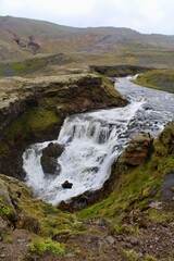 Majestic Icelandic Water fall with green moss and Lava rocks between cliff formation. damp fresh icelandic landscape with strong green and earth tones