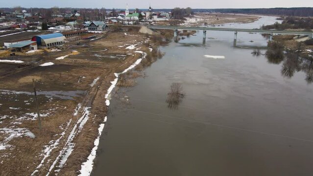 A pale river stream with gray water, the remains of snowdrifts on the shore. Spring, snow melts, dry grass, flood and river flood. Day, cloudy weather, soft warm light. UHD 4K