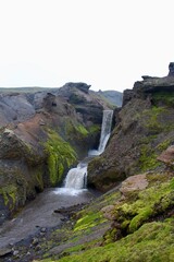 Majestic Icelandic Water fall with green moss and Lava rocks between cliff formation. damp fresh icelandic landscape with strong green and earth tones