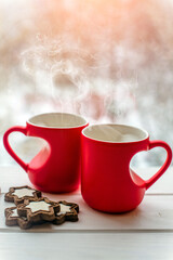two heart shaped mugs with tea on the background of a window in winter
