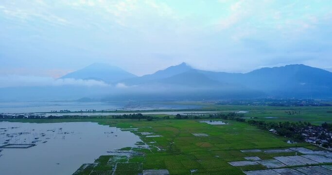 Drone shot of huge lake and rice field with mountain range on background. Many fish cage build on the lake - Rawa Pening Lake, Central Java, Indonesia