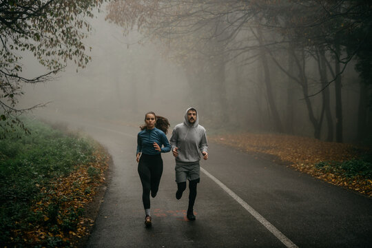 Fitness couple winter morning exercise at foggy mountain road.