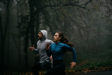 Woman and man in sports outfits in a full sprint on the forest road racing with each other. 