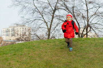Primary school pupil runs to or from school. Beautiful smiling boy in insulated jacket. Cold sizon.