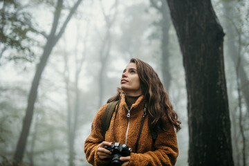 Anticipating a female hiker holding a photo camera and taking nature pictures during a foggy and...