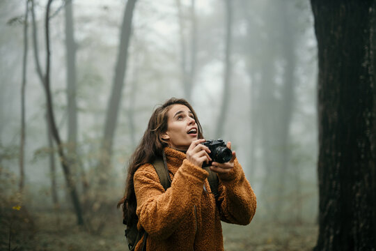 Anticipating a female hiker holding a photo camera and taking nature pictures during a foggy and rainy day.