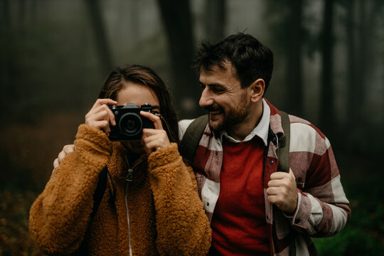 Loving and cheerful tourists spend vacation in the hills on a foggy day. A woman is holding a camera and taking a photo