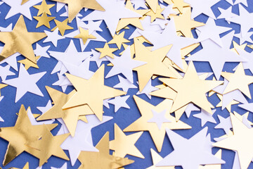 Golden stars and white confetty on blue background, selective focus. Festive holiday pastel backdrop.