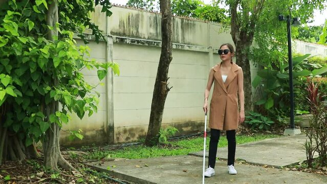 Blind asian woman needs fresh air and ozone from plants. Walks slowly on the sidewalk in the park using walking stick for leisurely walk. In a garden within the village where the air is fresh