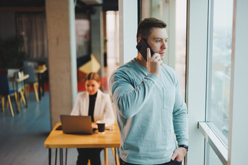 Business man, manager looking out of window in deep thought, standing at workplace with phone in...
