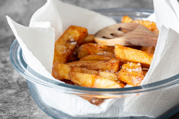Homemade chips in a glass dish with a paper towel and wooden spoon. On a dark stone background