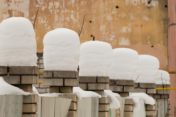 Beautiful, even, high columns of snow on brick pillars. An even row of small snowdrifts against the background of a shabby wall. Urban winter landscape. Cloudy winter day, soft light.