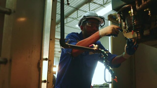 African American male technician worker inspects coolant pipes, autonomous steel cutters and drills, and ensures safety for efficient operation.