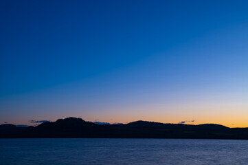 Fototapeta premium 夜明けの空は美しいグラデーションに山のシルエットが際立つ湖の風景。