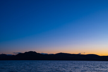 夜明けの空は美しいグラデーションに山のシルエットが際立つ湖の風景。